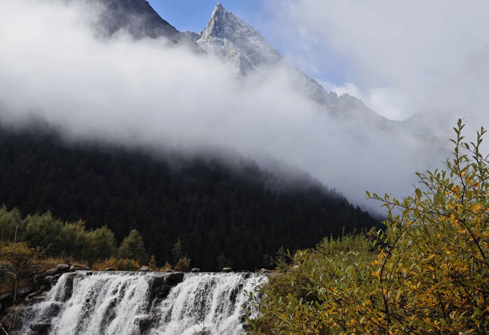 A waterfall under a clouded peak